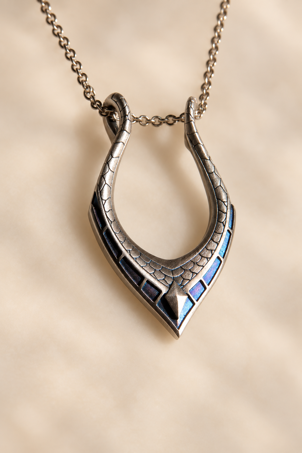 A silver horseshoe pendant necklace with blue detailing, resting on a white marble slab with a dark red fabric background.