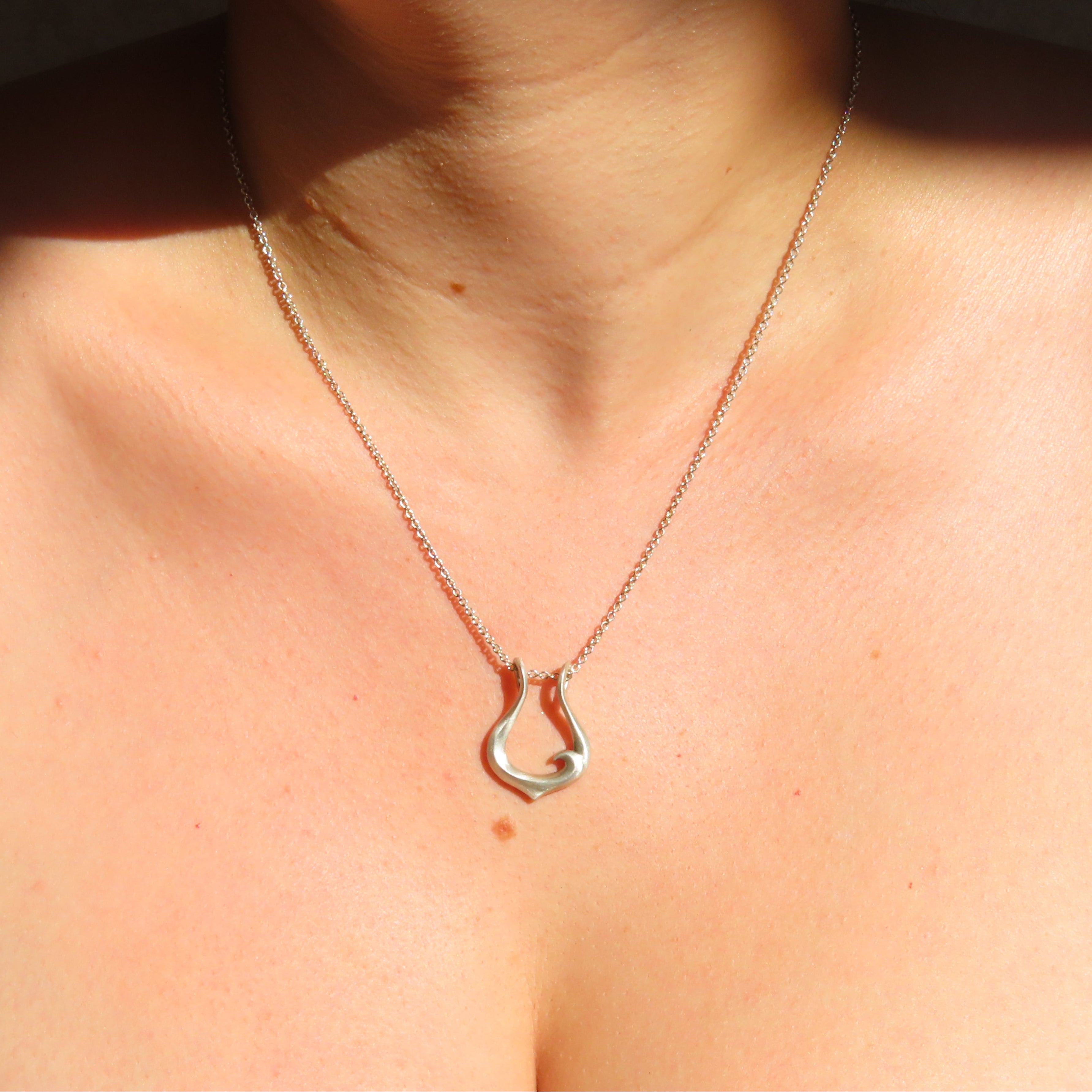 A close-up of a person's neck and upper chest wearing a delicate silver chain necklace with a small open teardrop-shaped pendant.